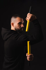 Vertical portrait of a serious young man is mastering the art of nunchaku over black background.