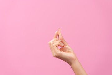 Gracefully, woman hand cradles a bottle of cod liver oil against a pink backdrop, representing...
