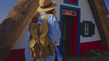 A girl travels in a hat and with a backpack and visits extraordinary traditional A-shaped houses in Santana in Portugal Madeira