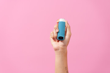 A professional image featuring a female hand holding an asthma inhaler with fingers against a soft pink isolated background, highlighting respiratory health and wellness. - obrazy, fototapety, plakaty