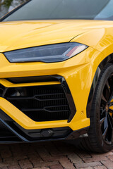 Cropped view of radiator grille and headlight on front bumper of yellow stylish car. Modern ventilation and cooling systems on massive off-road vehicle parked on paving stones