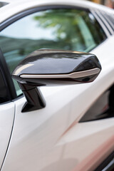 Close up view of side mirror placed on exterior of white luxury sport car with futuristic shape. Premium quality detailing design of unique deluxe class vehicle