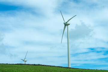 Wind turbines stand tall against a cloudy sky on Terceira Island, Azores. Capturing renewable...