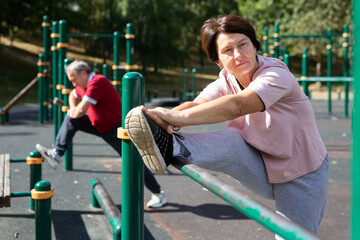 Elderly woman doing stretching on sports bars at an outdoor sports field