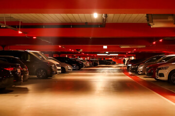 Underground parking garage with cars parked and illuminated by red lights, suitable for illustrating safety measures during emergencies or promoting secure parking facilities. Blurred