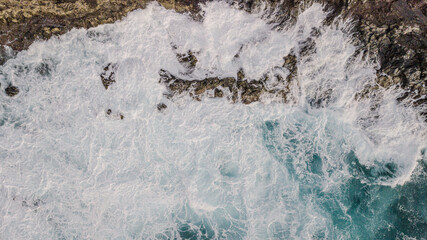 View from drone of Atlantic ocean waves meet with underwater pointed rocky. Blue rough sea with big waves with foam crashing against the rocks, south of Tenerife, Canary island