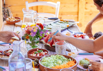Inviting colorful table in outdoors with drinks and vegetarian food and hands of people sharing brunch