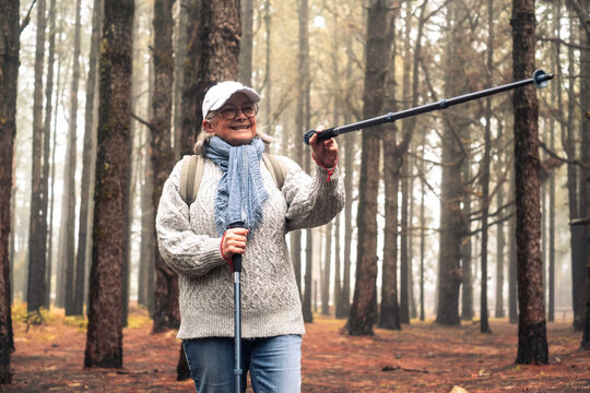 Active happy senior woman with backpack walking in mountain forest on a foggy day with the help of poles enjoying nature, freedom and free time. Forest background with bare trees