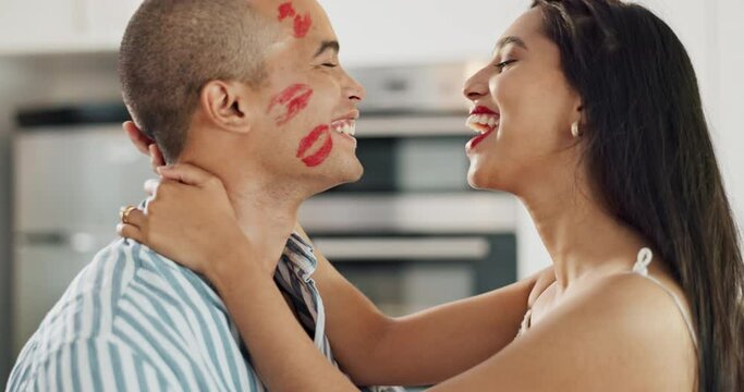 Happy couple, love and kiss with lipstick for fun date and playful at home in intimacy, romance and valentines day. Lover, woman and man in kitchen or house with lip print on cheek for anniversary