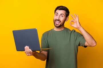 Fototapeta premium Photo portrait of handsome young guy hold netbook show okey symbol dressed stylish khaki outfit isolated on yellow color background
