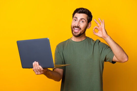 Photo portrait of handsome young guy hold netbook show okey symbol dressed stylish khaki outfit isolated on yellow color background