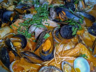 Selective focus on mussels in tomato sauce with clams and shrimp and green parsley on top