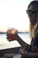 giovane donna beve un cocktail al tramonto in riva al mare