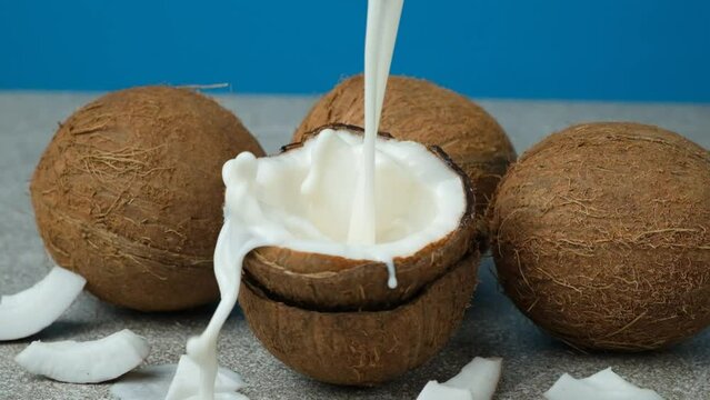 Healthy vegan coconut milk pouring into half a coconut, splash of milk slow motion