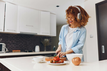 Woman wearing headphones preparing a healthy snack in the kitchen with slices of bread and tomato...