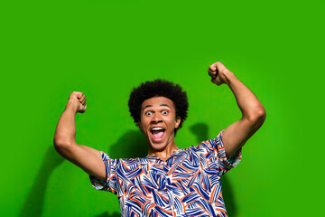 Photo of good mood impressed man dressed print shirt rising fists screaming yeah isolated green...