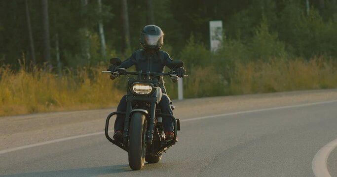 Brutal woman in black helmet riding modern motorbike at country road. Motorcyclist racing his motorcycle on asphalt road. Lady driving bike during trip at sunset lighting, concept of adventure