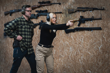 A young girl is training to shoot a pistol with an instructor at a shooting range.