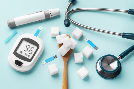 Sugar cubes in spoon with blood glucose meter, lancet and stethoscope on blue background