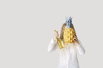 Summer conceptual photo woman hide head in yellow paper pineapple. Girl with long hair holding bottle champagne sparkling wine Summer party, celebration, vacation concept, positive mood.