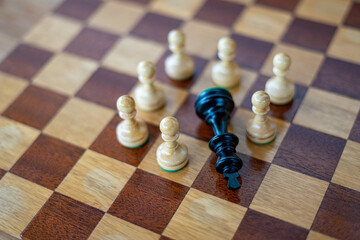 Defeated black chess king surrounded by white pawns on wooden chess board