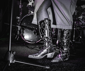 Cowboy boots close-up on female singer with mic stand and drums at a hoedown.