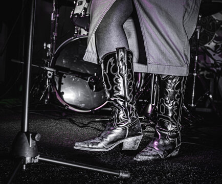 Cowboy boots close-up on female singer with mic stand and drums at a hoedown.