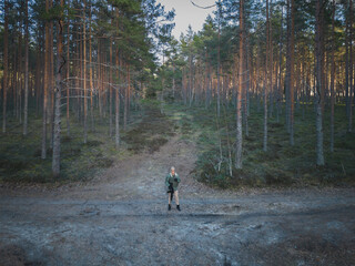 A military girl with a rifle with a silencer in a pine forest. Drone photo.