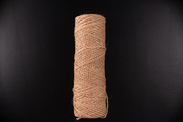 A brown rope is sitting on a black background. The rope is long and thin, and it is made of natural fibers. The image has a simple and minimalistic feel