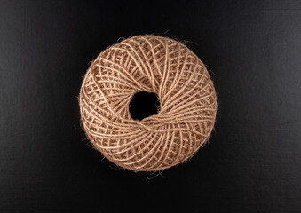 A brown ball of yarn is sitting on a black surface. The yarn is twisted and knotted, giving it a...