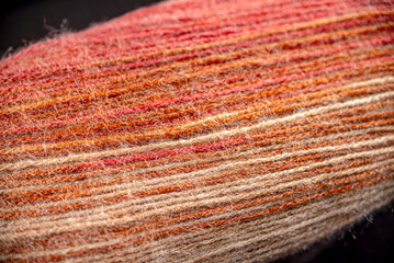 A close up of a piece of yarn with a red stripe. The yarn is knotted and has a fuzzy texture