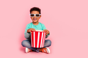 Full length photo of adorable little boy sit floor eat popcorn watch movie dressed stylish cyan garment isolated on pink color background