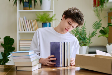 Satisfied young male customer unpacking cardboard box with online purchases, new books