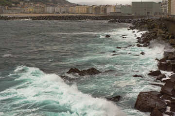 Obraz premium Ocean waves crash against the rocky shore. San Sebastian, Spain. Cloudy spring day