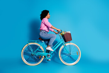 Full length side profile photo of active girl dressed shirt jeans riding bike look at sale empty space isolated on blue color background