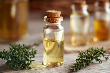 A transparent bottle of aromatherapy essential oil with fresh thyme on a table