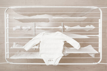 White clean baby bodysuit on drying rack at home room. Closeup. Newborn clothes washing. Top down view.