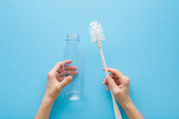 Young adult woman hands holding white brush and transparent plastic bottle on light blue table background. Pastel color. Point of view shot. Closeup. Top down view.
