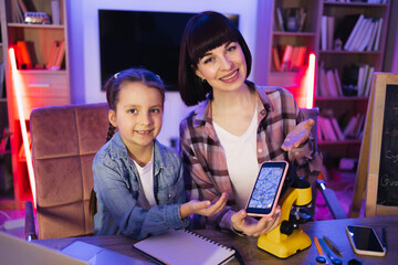 Caring Caucasian mother teaching her little daughter how to examine plant cells using electronic microscope at home laboratory. Biological scientist education moment during parenthood, nightlife. - Powered by Adobe