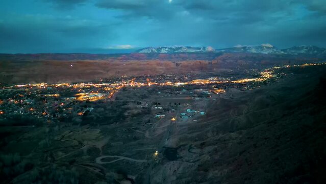 aerial shot of moab utah with red mountains behind the city during sunset