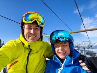 Cute family of skiers make selfie on chairlift, mountain behind - 773066895