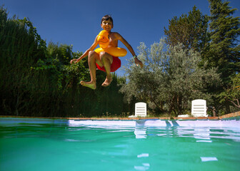 Sunny poolside fun with jumping teen boy captured in motion - 773067014