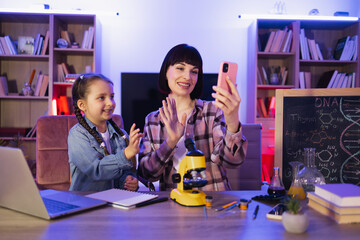 Attractive woman and little girl using using phone to video stream science blog. Happy mother with...