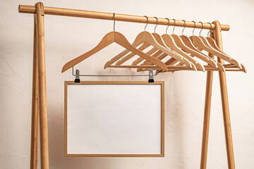 A set of wooden hangers on a bamboo garment rack with a blank white frame hanging among them.