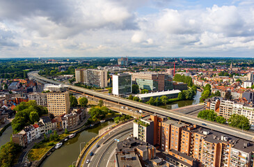 Ghent, Belgium. Autobahn with a bridge over the canal. Residential and industrial areas. Panorama of the city. Summer day, cloudy weather. Aerial view