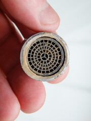 Hand is holding a chrome faucet aerator covered with lime scale. Faucet contaminated with calcium. Limescale on tap mixer.
