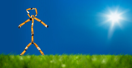 conceptual stick man of cigarette butts on green grass landscape over sunny sky