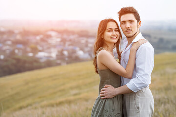 Courageous man and positive woman pose standing on hill slope top overlooking large village in cloudy weather, sunlight. Concept of harmony in relationships and love