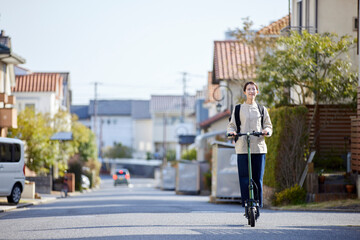 住宅街を電動キックボードで移動する日本人の女性 - obrazy, fototapety, plakaty