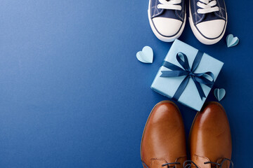 Celebrating father's day: Overhead view of festive blue gift and gentleman's shoes with hearts on a deep blue background with ample space for text